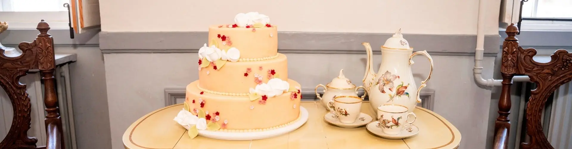 Bryllupskage i tre etager med blomster ved et kaffebord med porcelæn